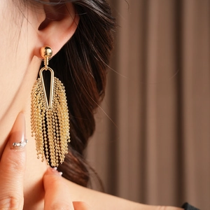 Close-up of golden tassel drop earrings featuring a beaded triangle frame on model