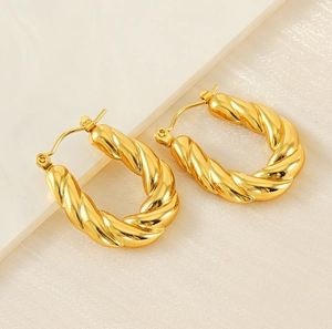 Macro view of gold U-shaped twist hoop earrings on a marble and silk background