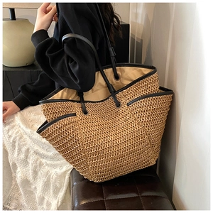 Detail of a large straw beach tote with black leather straps and premium woven texture