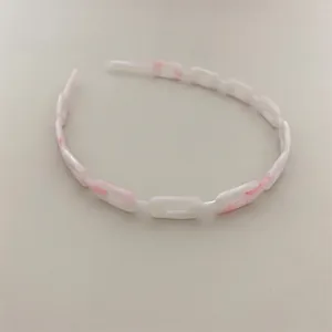 Detail of pink and white marble acetate chain-link headband with a minimalist aesthetic
