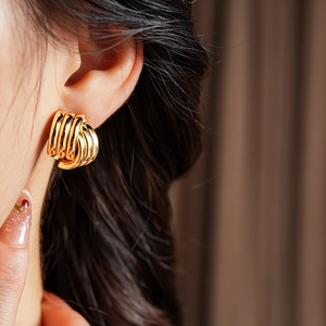 Close-up of model wearing gold geometric layered hoop earrings with a metallic finish