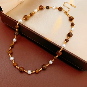 Detail of tiger eye and pearl necklace with golden clasp on brown leather surface