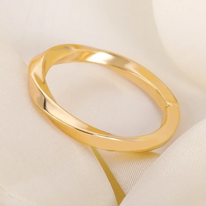 Detail view of a gold-plated twisted mobius ring resting on elegant cream silk fabric