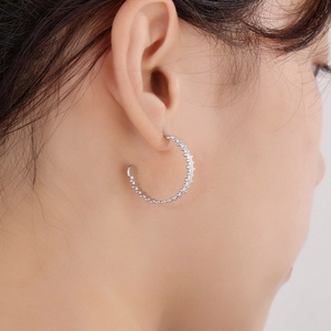 Close-up of C-shaped silver hoop earrings with textured finish on a female model