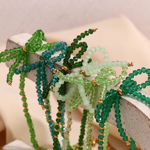 Macro shot of green faceted crystal beads and bow tie pendant on stainless steel chain