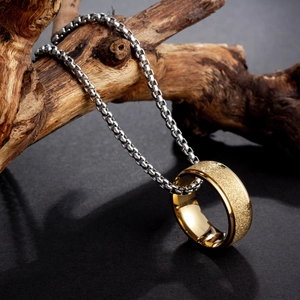 Nahaufnahme eines goldenen Rings an einer silbernen Box-Kette vor rustikalem Holz
