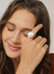 Detail of a large round mother of pearl ring with gold metal finish on model hand