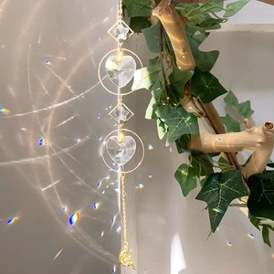 Detail of star and heart crystal suncatcher reflecting rainbow light on a wooden branch