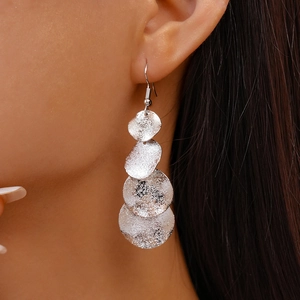 Détail de boucles d'oreilles géométriques argent mat portées par un mannequin avec élégance
