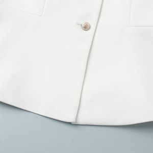 Detail of white twill fabric vest featuring a golden embossed decorative button close-up