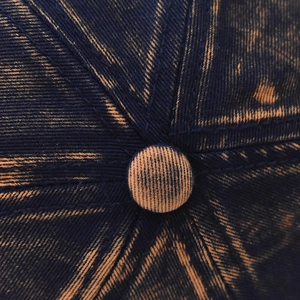Macro detail of vintage acid-wash denim baseball cap crown with button and stitching