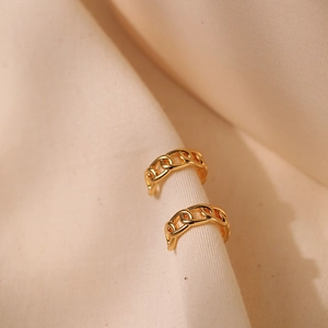 Golden chain link earrings on beige fabric background with minimalist metallic texture