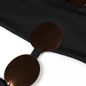 Detail of black beach dress featuring bronze metal ring accents and textured fabric