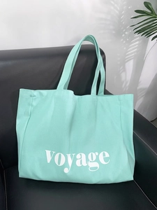 Detail of mint green canvas tote bag with Voyage lettering on a leather background