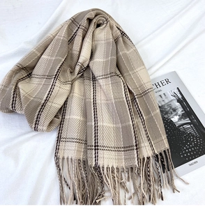 Detail of classic plaid scarf with fringe on a white textured background with a book