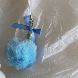 Close-up of blue plush fur ball pendant with ribbon bow and silver heart charm keychain
