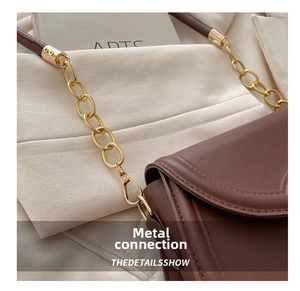 Detailed view of brown leather bag with golden metal chain strap on white blazer