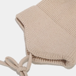 Détail du bonnet à oreilles en maille côtelée beige avec textures et liens à nouer