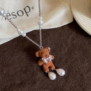 Détail du pendentif ours floqué avec jambes en perles et nœud strass sur chaîne argentée