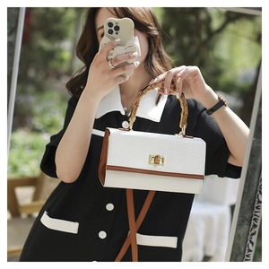Close-up of white crocodile pattern handbag with classic bamboo handle and brown leather trim
