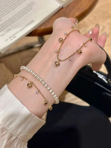 Detail of layered gold heart bracelet and white pearl strand on model wrist