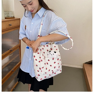 Close-up of white strawberry corduroy tote bag featuring a cute plush bear charm