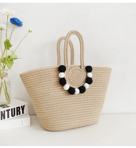 Detail of handmade straw tote bag with decorative black and white pom-pom charms