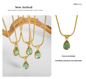 Close-up of a green teardrop emerald pendant on a polished gold snake chain necklace