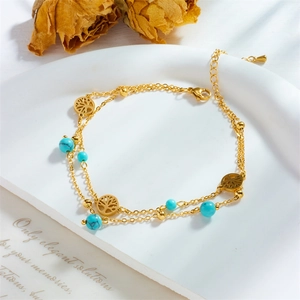 Double-layer gold anklet with turquoise beads and tree of life pendants on white tray