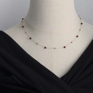 Détail macro d'un collier chaîne dorée fine avec perles rouge grenat sur mannequin