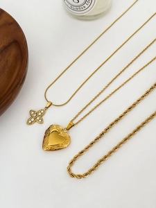 Détail de colliers dorés superposés avec croix en strass et médaillon coeur gravé