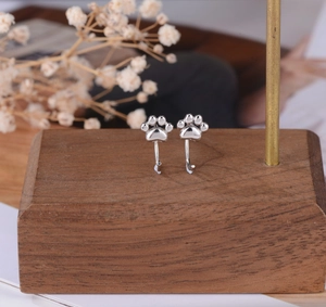 Detailed view of silver cat paw hook earrings on a rustic wooden display stand