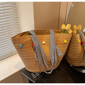 Detail of woven tote bag with colorful pom-poms and striped handles in natural sunlight