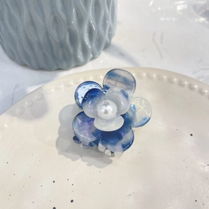 Detailed view of a blue and white acetate flower hair claw clip with a center pearl detail
