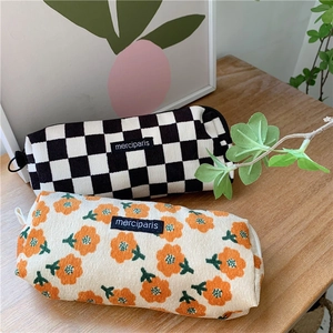 Corduroy zipper pencil cases in checkerboard and floral patterns on a wooden desk