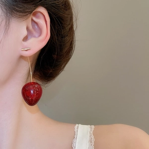 Détail de boucles d'oreilles cerises rouges avec tiges dorées portées par un modèle