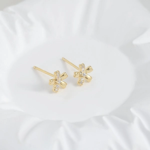 Close-up of gold-tone flower stud earrings with white zircons on a white ceramic tray