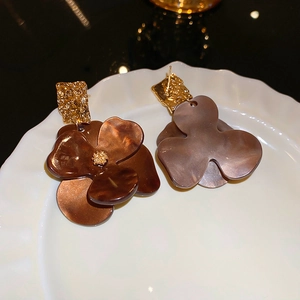 Detail of amber acrylic flower earrings with golden texture posts on a ceramic plate