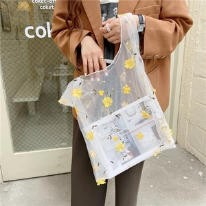 Detail of white mesh handbag with yellow 3D floral embroidery carried by a model