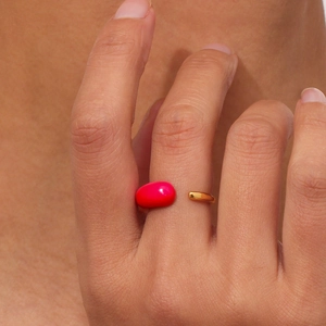 Macro shot of gold adjustable teardrop ring with pink enamel detail on model finger