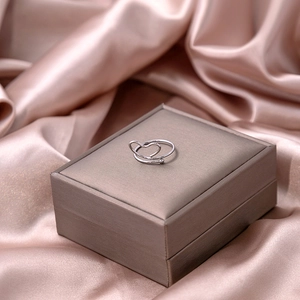 Macro detail of silver heart-shaped knot ring displayed on champagne silk jewelry case