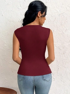 Rear view of slim fit wine red sleeveless top paired with blue jeans against a textured wall