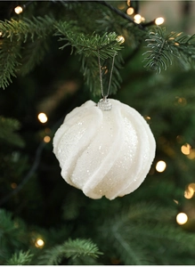 Nahaufnahme weißer Weihnachtskugel mit Pailletten und Plüsch an grünen Tannenzweigen