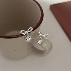 Silver bow heart earrings hanging on a beige ceramic mug with a cozy home backdrop