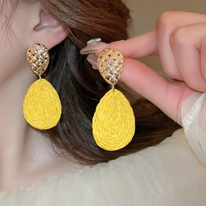Close-up of yellow woven teardrop earrings with textured gold metal accents on a model