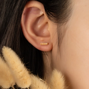 Détail de boucles d'oreilles dorées rectangulaires avec cinq cristaux orange portées