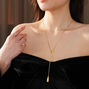 Detail of a gold plated teardrop pendant necklace on model with black velvet outfit