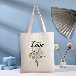 Cream canvas tote bag with daisy floral print and text hanging in a studio setting