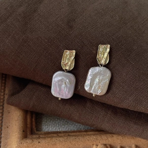 Close-up of baroque freshwater pearl earrings with textured gold plating on brown fabric