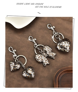 Detailed view of heart and bow leopard print keychains with silver hardware on tray
